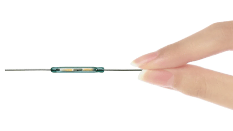 A close-up of a hand gently holding a thin medical device with a cylindrical component in the middle, possibly utilizing Standex Detect Reed Sensors, positioned between two fingers against a white background. by Standex Detect