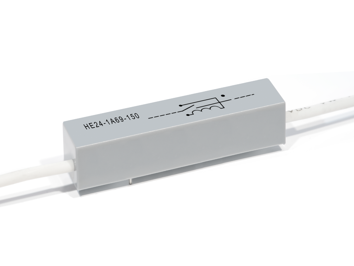 A gray rectangular HE Series Reed Relay features a white cable attached at each end, labeled HE24-1A69-150, and displays a printed electrical schematic symbol on its surface. by Standex Detect