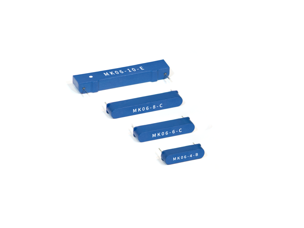 Four blue rectangular MK06 Series reed switch components of varying sizes are arranged in a diagonal row on a white background. Each component has a code printed in white text on its surface. by Standex Detect